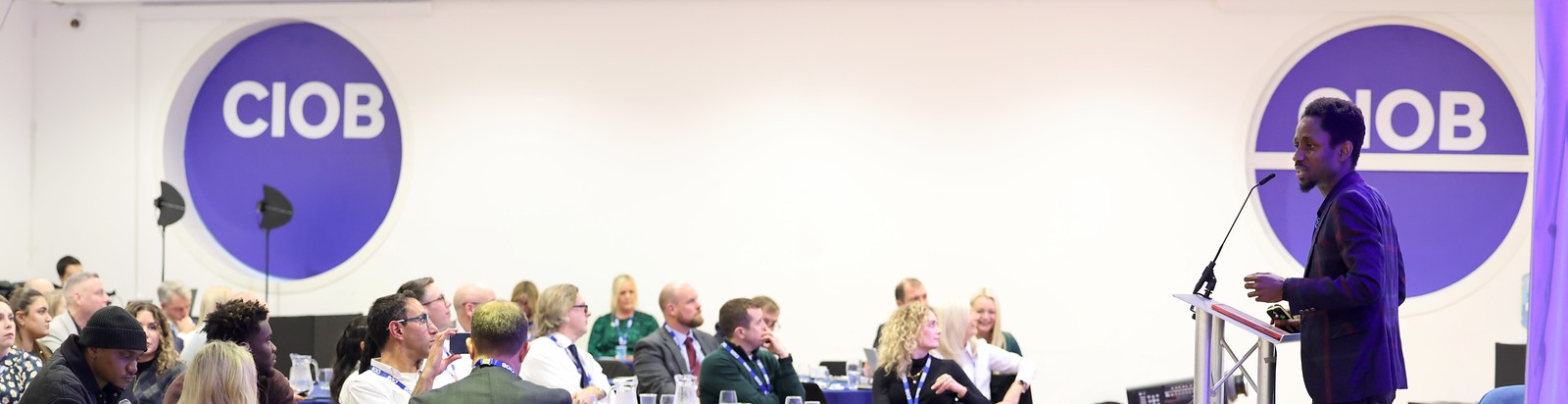 Kufre Antia speaking at a CIOB conference, addressing a seated audience beneath the CIOB logo